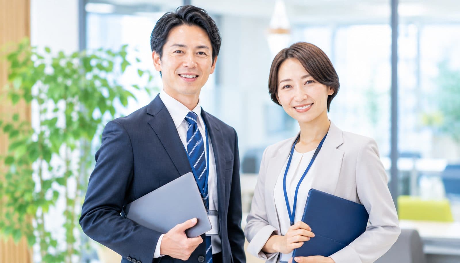 明るいオフィスで、ノートパソコンを抱えて並んで立っている男女ふたり