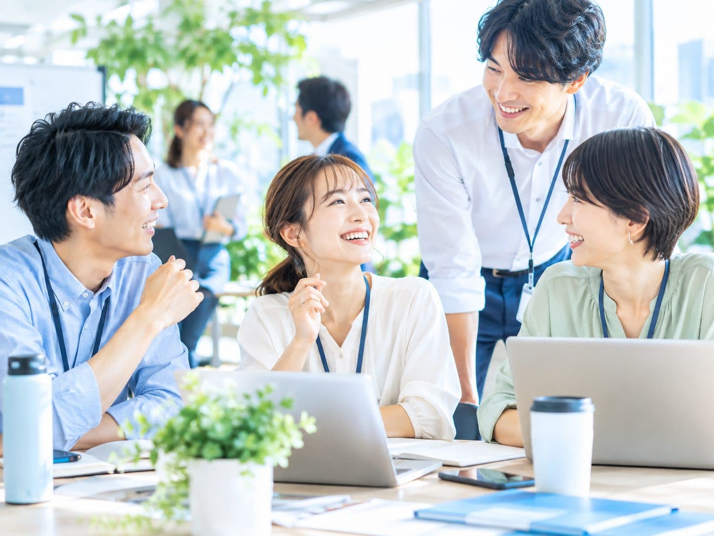明るいオフィスで、ノートパソコンを前に笑顔で話している4人