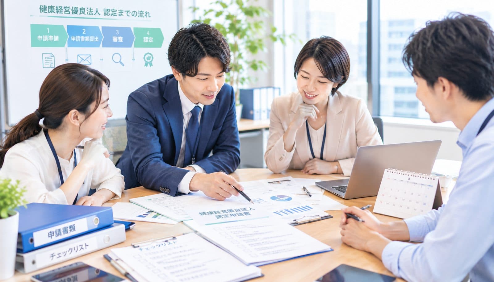 会議室で、健康経営優良法人の認定までの流れを示したボードを前に、申請書類とチェックリストを広げて打ち合わせをしている4人